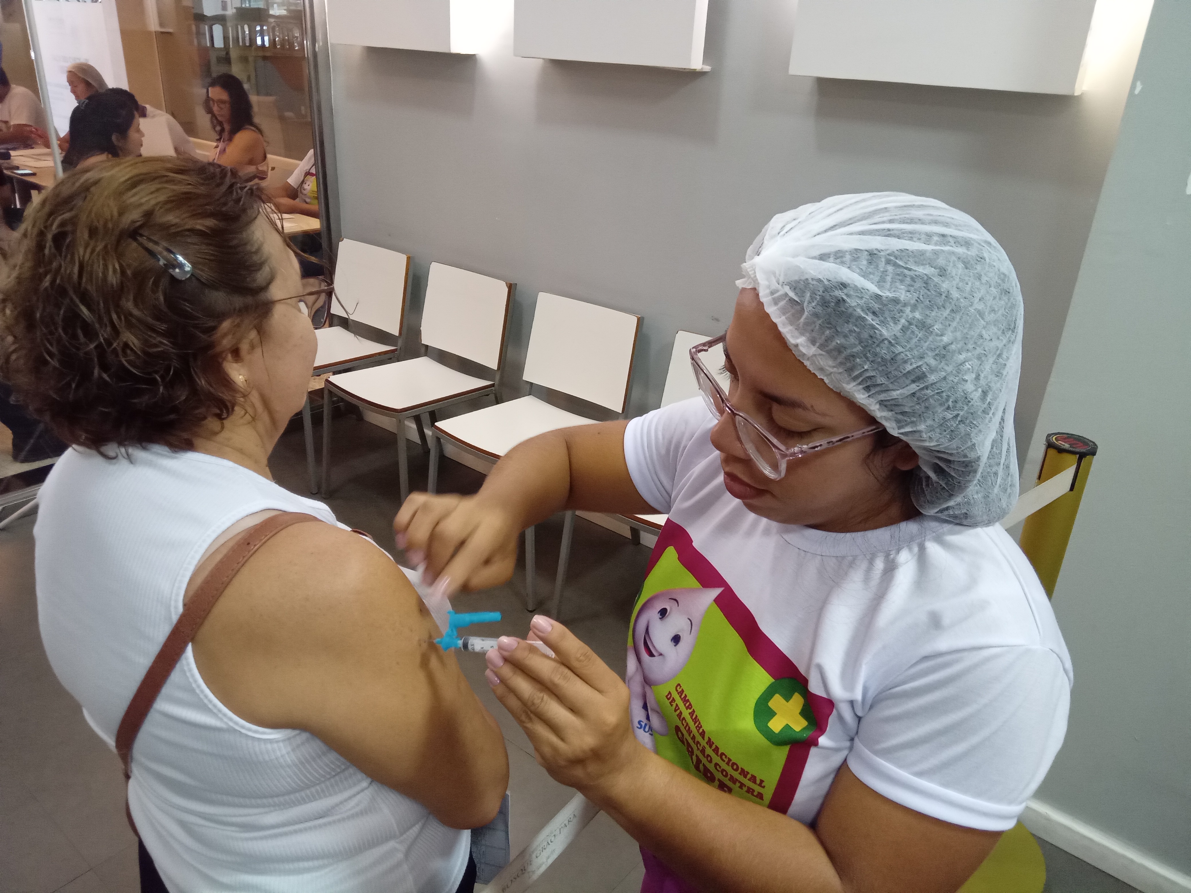 Uma mulher sendo vacinada no braço por uma profissional da saúde