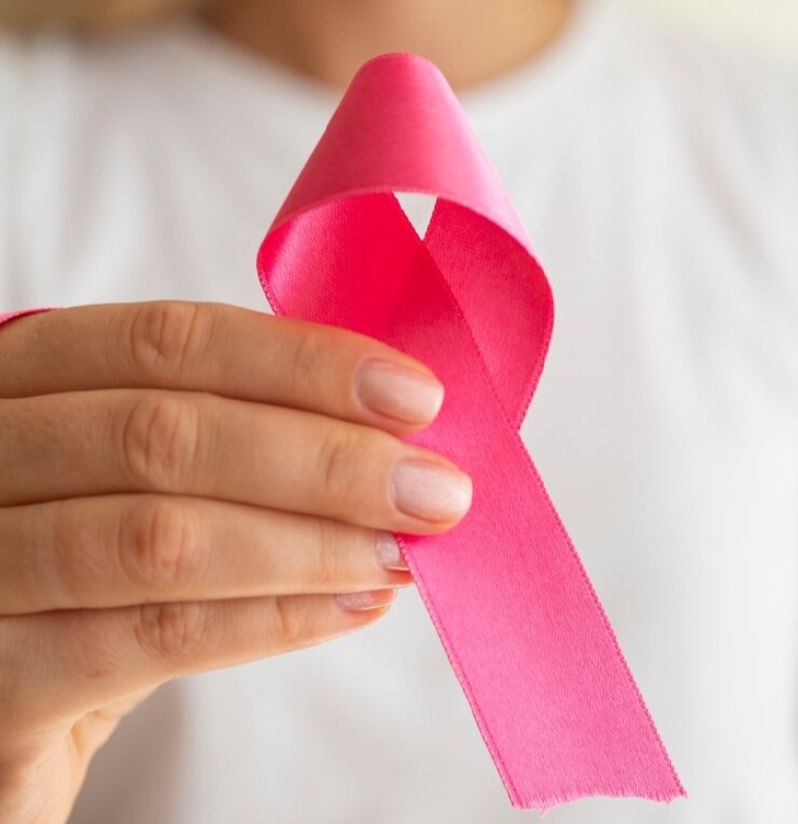 Em destaque na foto - um laço rosa segurando por uma mão de uma mulher em alusão a campanha de Outubro Rosa