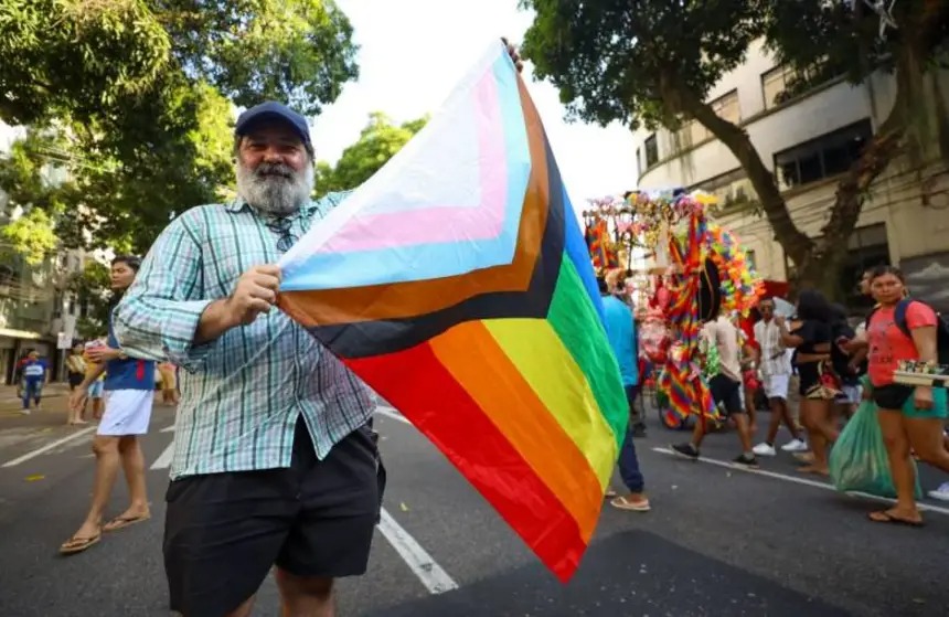 Um senhor segurando uma badeira LGBTQIA+ na rua publica.