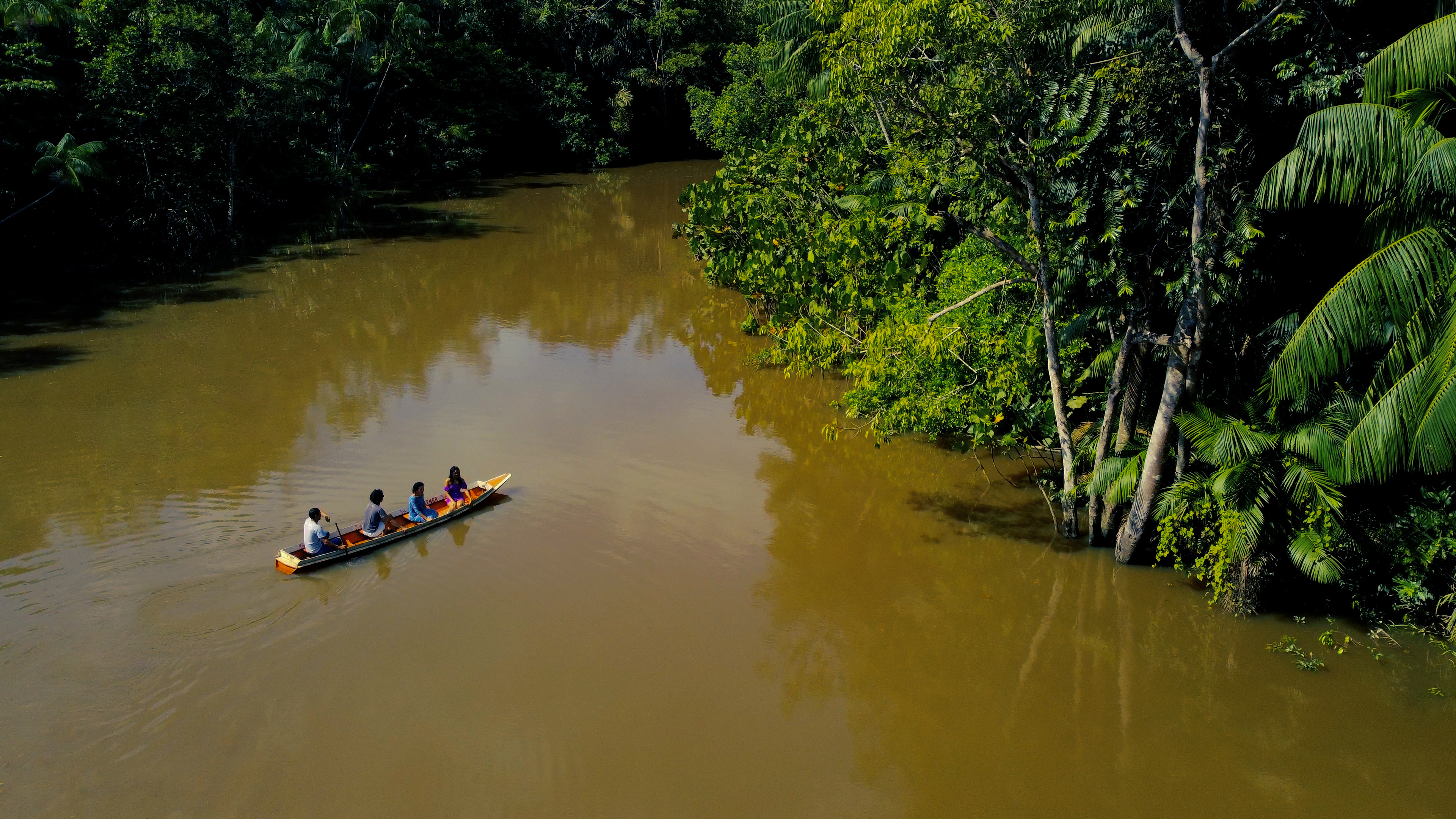 Quatro pessoas em uma canoa por um rio na amazônia. Imagem de Divugação da Obra