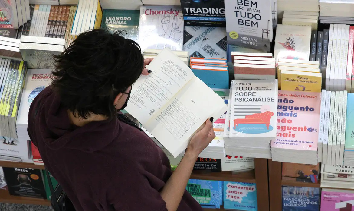 Uma mulher lendo um livro em meio a tantos outros livros numa estante