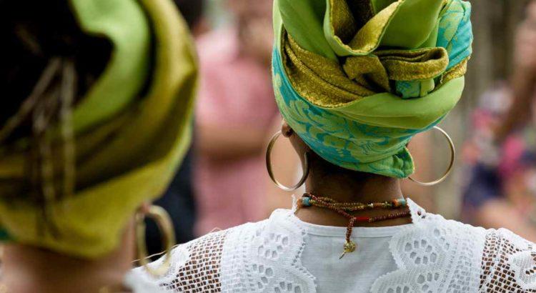 Mulher negra de costas usando um turbante, argolas e um cordão