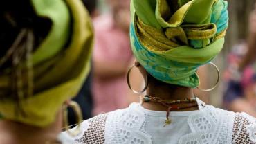 Mulher negra de costas usando um turbante, argolas e um cordão