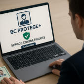 Homem em frente a um notebook ligado sobre Uma mesa. Na tela do PC há uma imagem onde se lê "BC PROTEGE + SERVIÇO CONTRA FRAUDES".